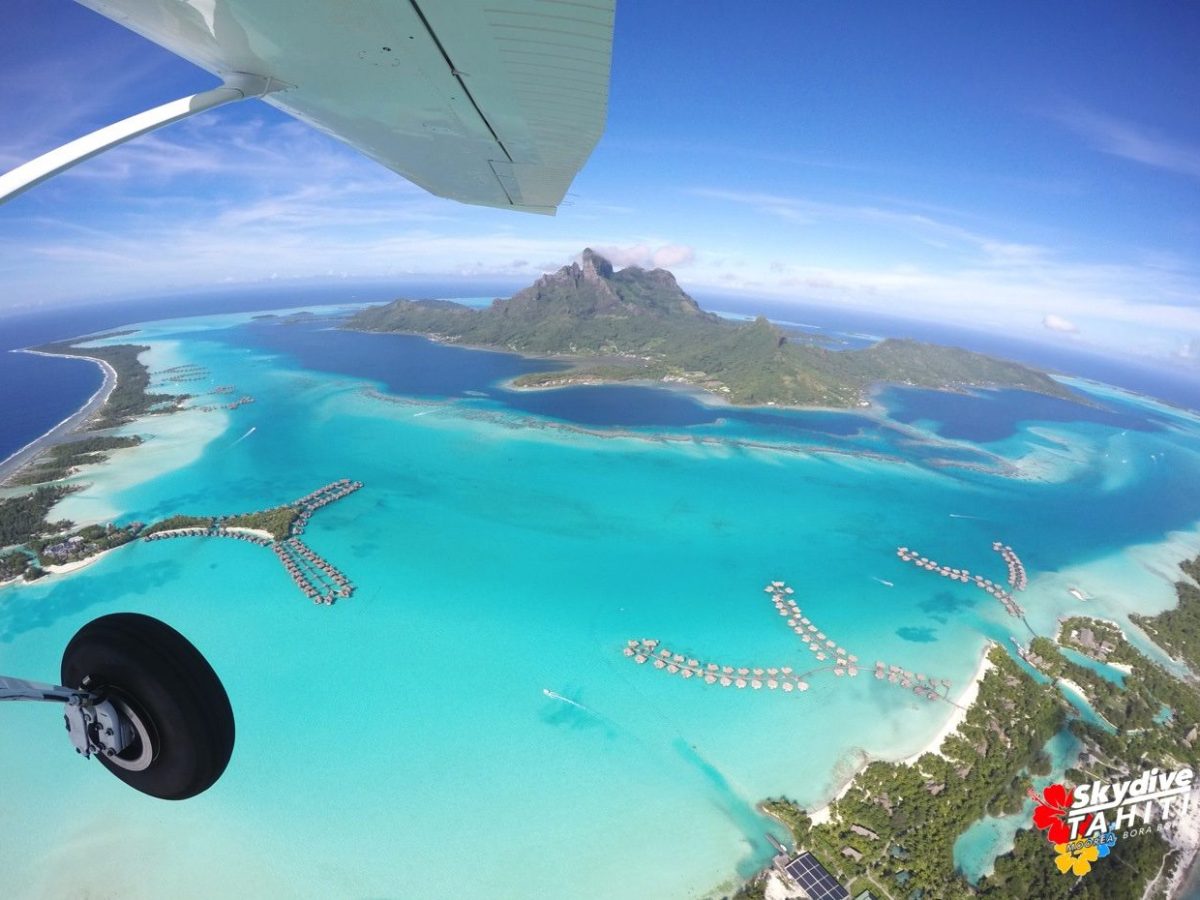 Aerial view of tropical island and turquoise lagoon with overwater bungalows.