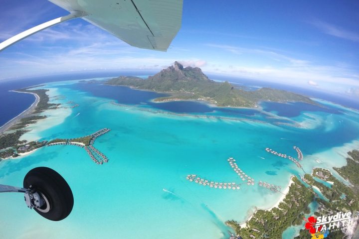 Aerial view of tropical island and turquoise lagoon with overwater bungalows.