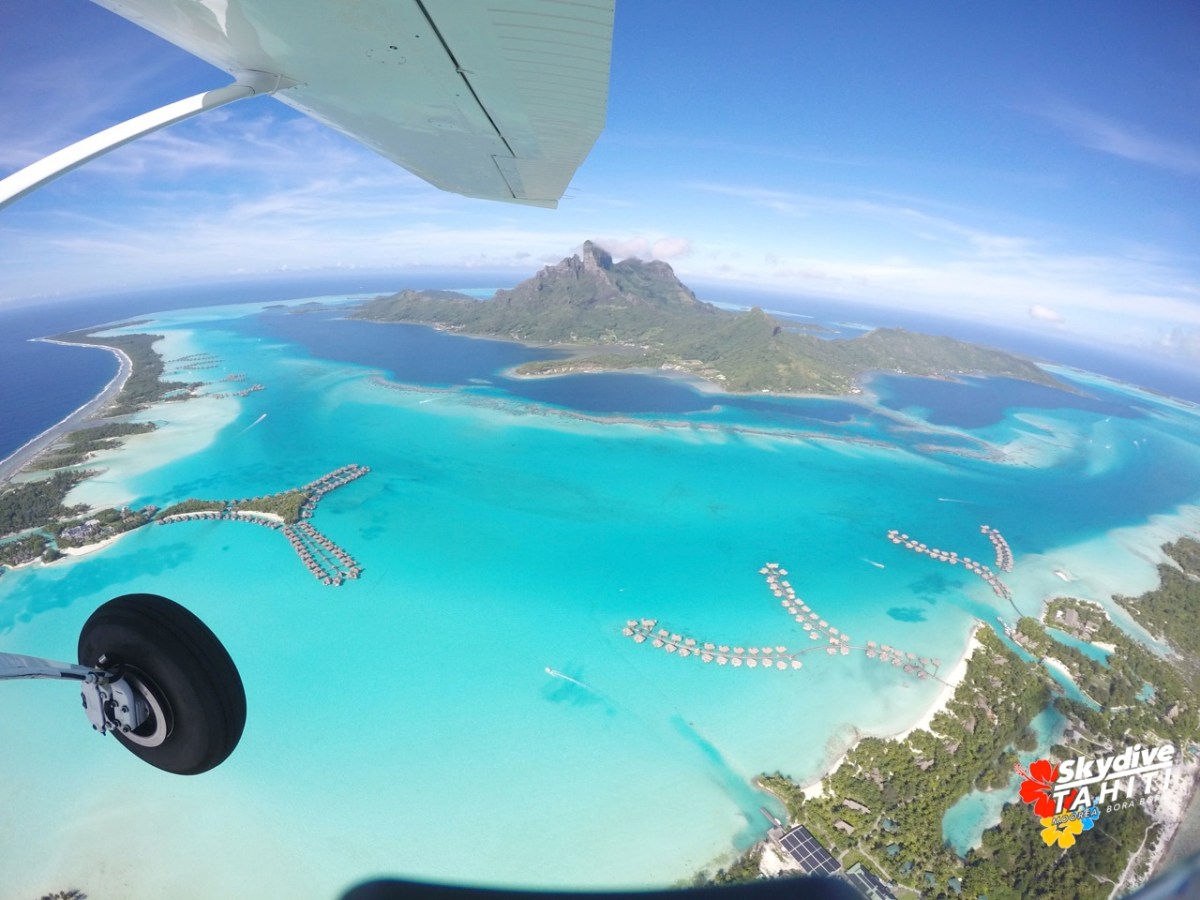 Aerial view of tropical island and turquoise lagoon with overwater bungalows.