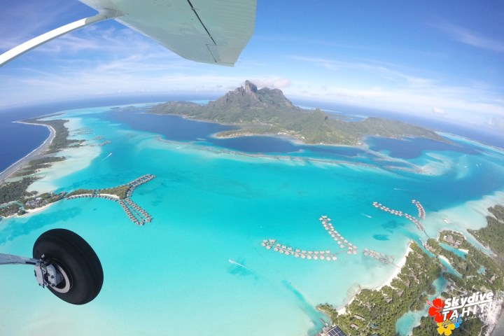 Aerial view of tropical island and turquoise lagoon with overwater bungalows.
