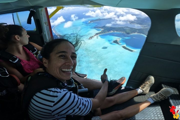 People in a plane preparing to skydive over bright blue ocean and islands below.