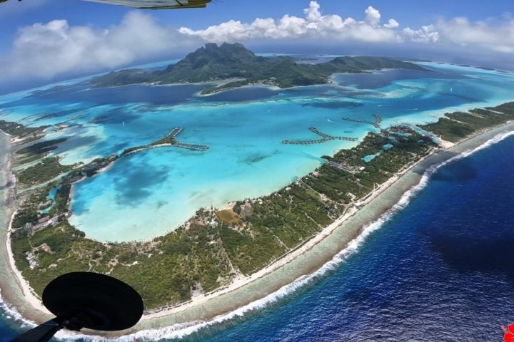 Aerial view of an island with lush greenery and turquoise lagoons surrounded by sea.