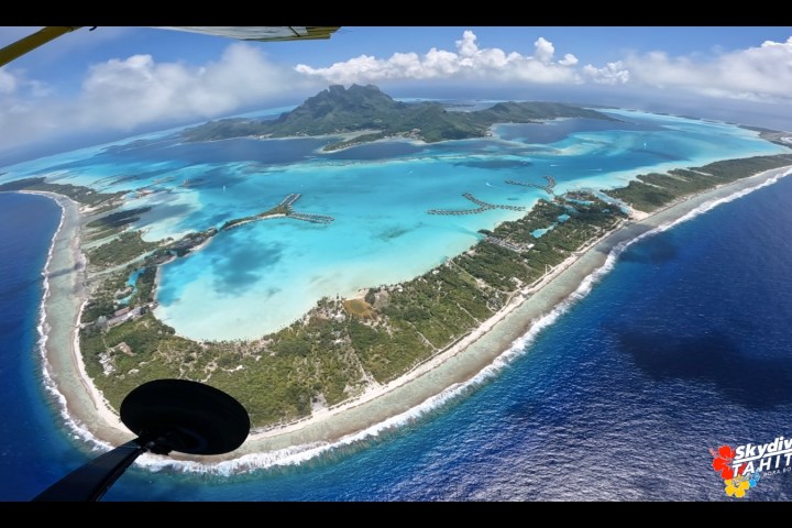 Aerial view of an island with lush greenery and turquoise lagoons surrounded by sea.