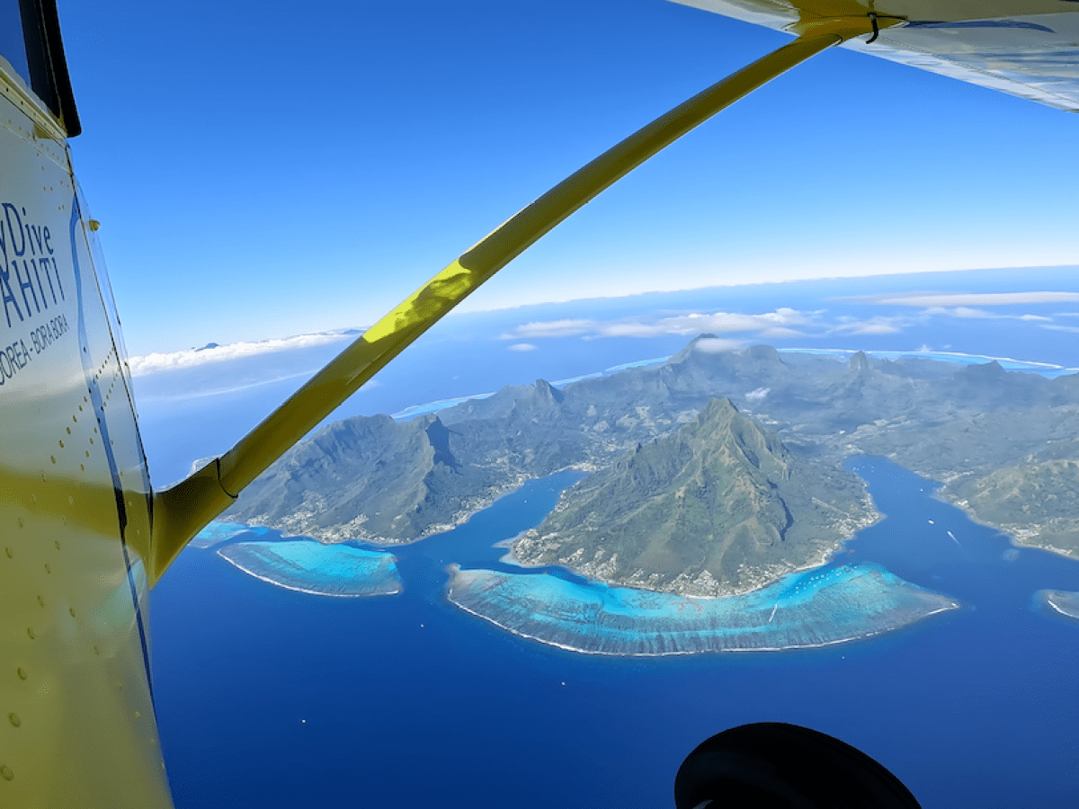 View of tropical island from airplane window with blue ocean and green mountains.
