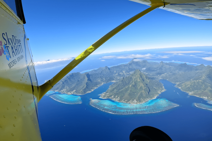 View of tropical island from airplane window with blue ocean and green mountains.