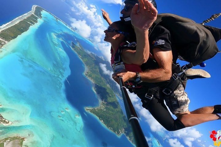 Two people tandem skydiving over turquoise waters and lush islands.