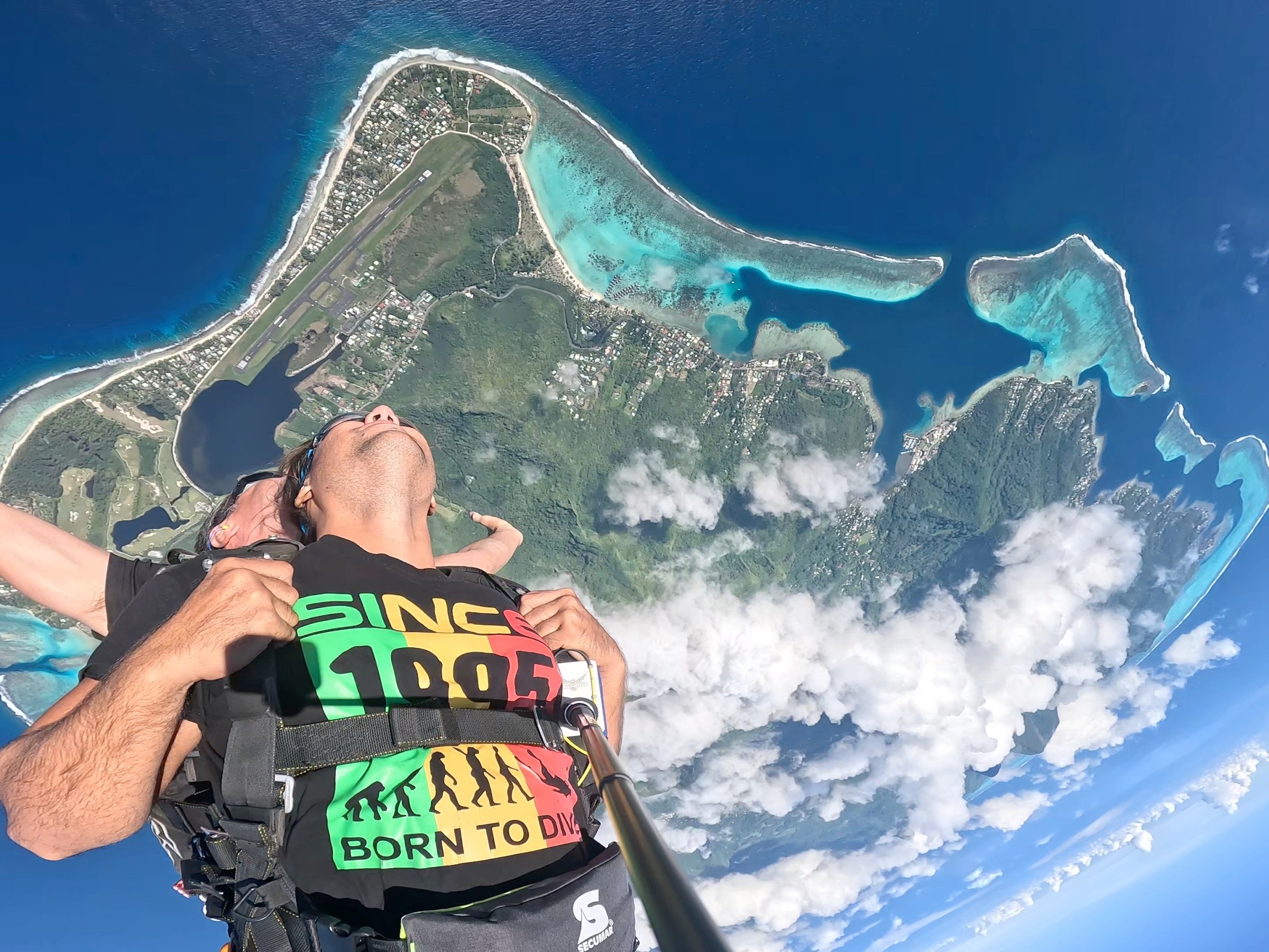 Two people tandem skydiving over a tropical island and turquoise sea.