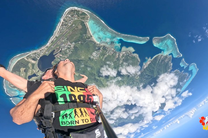 Two people tandem skydiving over a tropical island and turquoise sea.