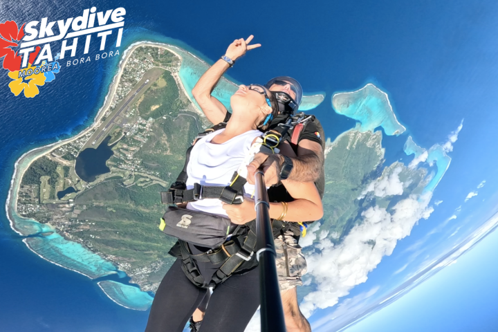 Tandem skydiving over island with ocean and clouds, Skydive Tahiti logo visible.