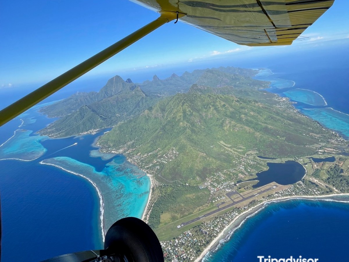 Aerial view of a tropical island with an airplane wing overhead and award logo in corner.