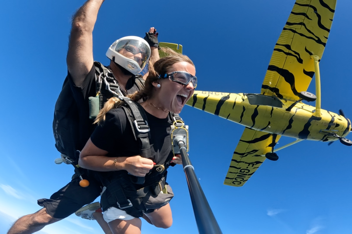 Two people tandem skydiving near a yellow tiger-striped airplane.