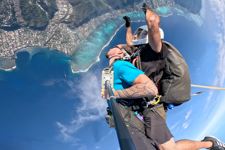 Tandem skydive over coastline with blue ocean and city below.