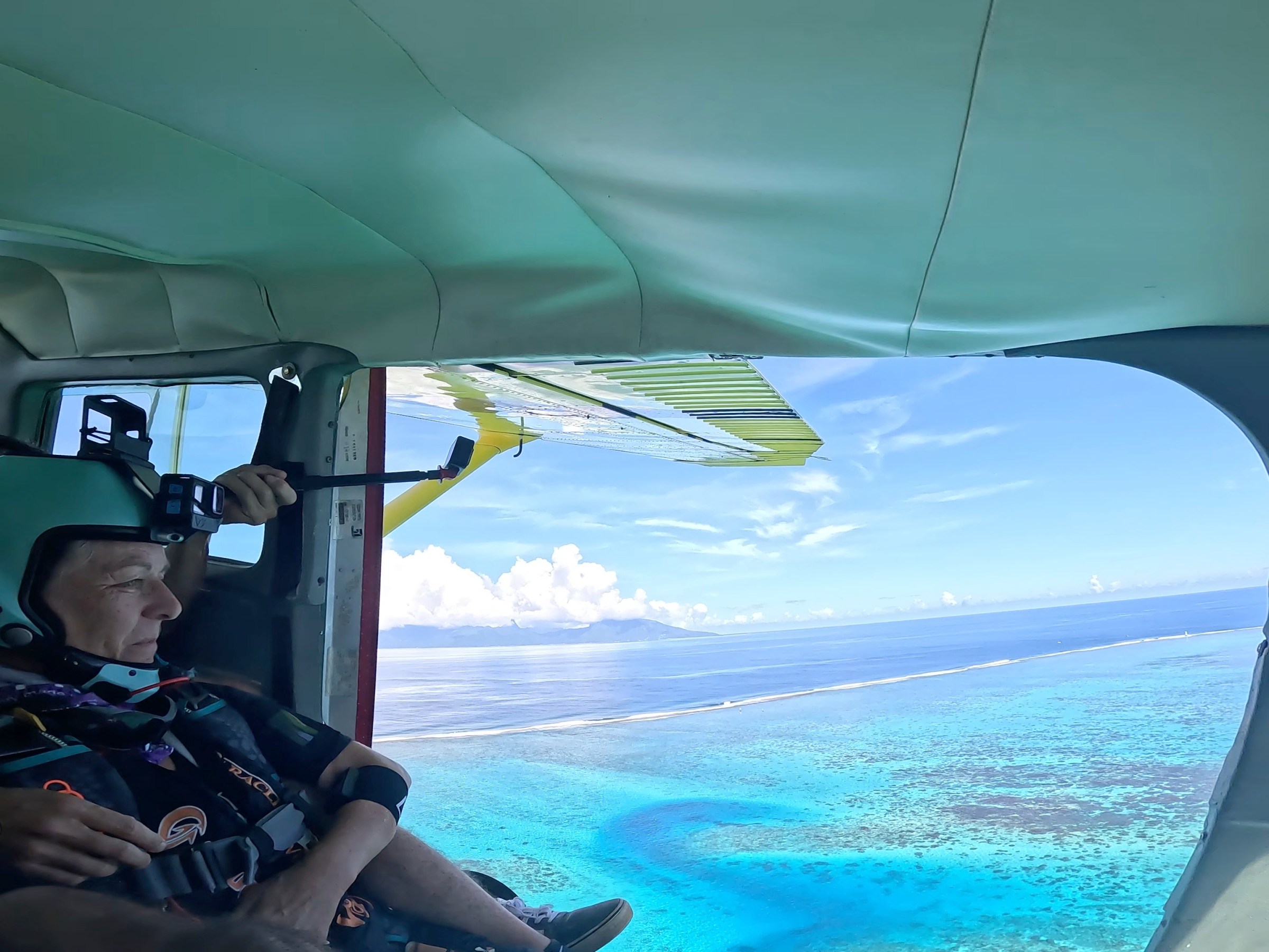 Skydivers prepare to jump from a plane over a blue ocean with islands in the distance.
