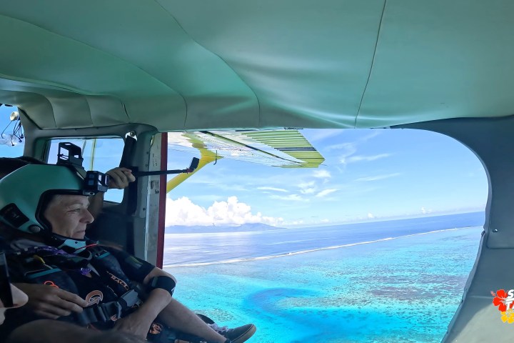 Skydivers prepare to jump from a plane over a blue ocean with islands in the distance.