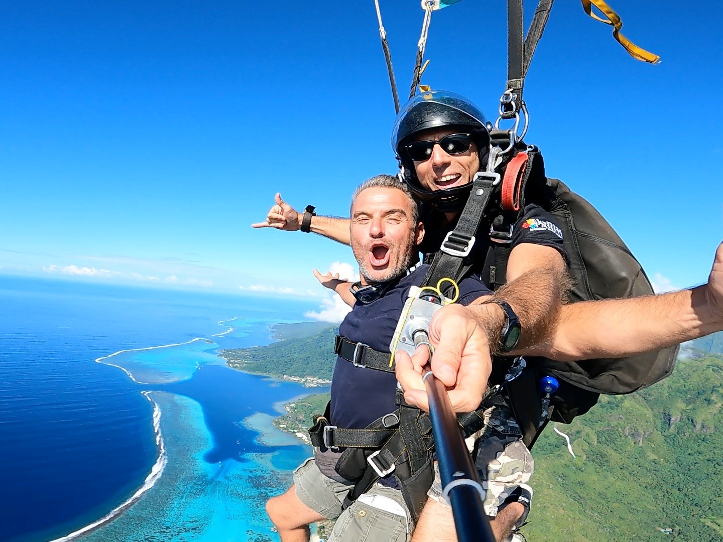 Two people tandem skydiving above an island with clear blue sky and ocean view.